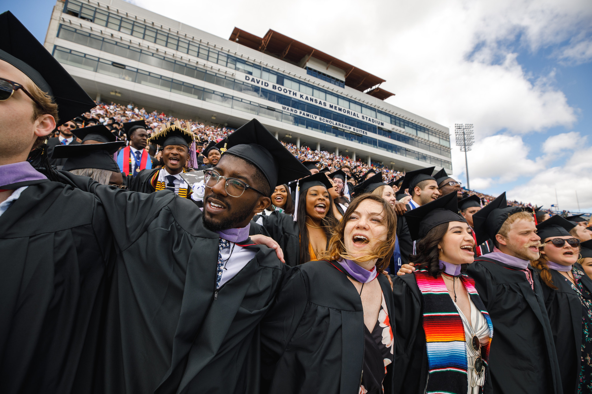 Memorial stadium filled with graduates with their arms around one another