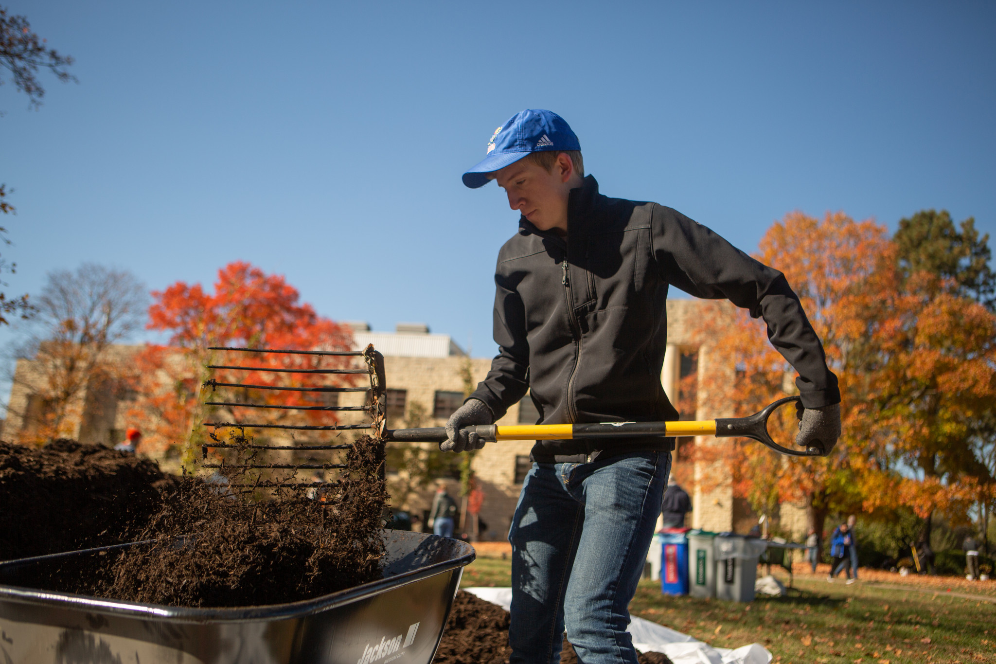 A student uses a gardening spade to move dirt on campus